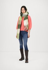 Lys korallfarget teksturert genser, grønt og hvitt rutete skjerf med frynser, mørkeblå slim fit jeans og brune knelange støvler med spenner.