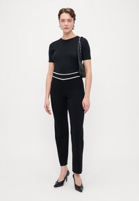 Top negru, ajustat, cu mâneci scurte și pantaloni cu talie înaltă asortați, având un accent orizontal alb la talie. Pantofi cu toc negri și geantă neagră.