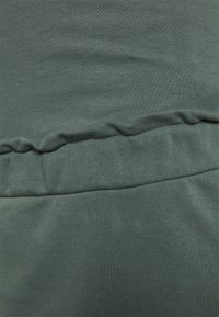 Tecido verde com uma textura suave, apresentando uma cintura franzida e detalhes em malha, criando uma aparência confortável e ajustada.