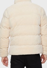 Chaqueta tipo puff en color crema, hecha de tela de felpa con rayas horizontales. Cuenta con un cuello alto y puños elásticos para un ajuste ceñido.