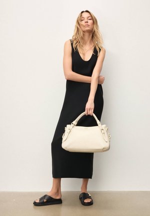 Vestito nero senza maniche, borsa beige con texture e dettagli dorati, e sandali neri con cinturini incrociati, su sfondo neutro.