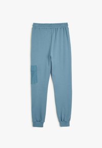 Blå svedbukser lavet af blødt stof, med en elastisk talje, manchetter ved anklerne og en sidelomme i cargo-stil i et kontrasterende materiale.