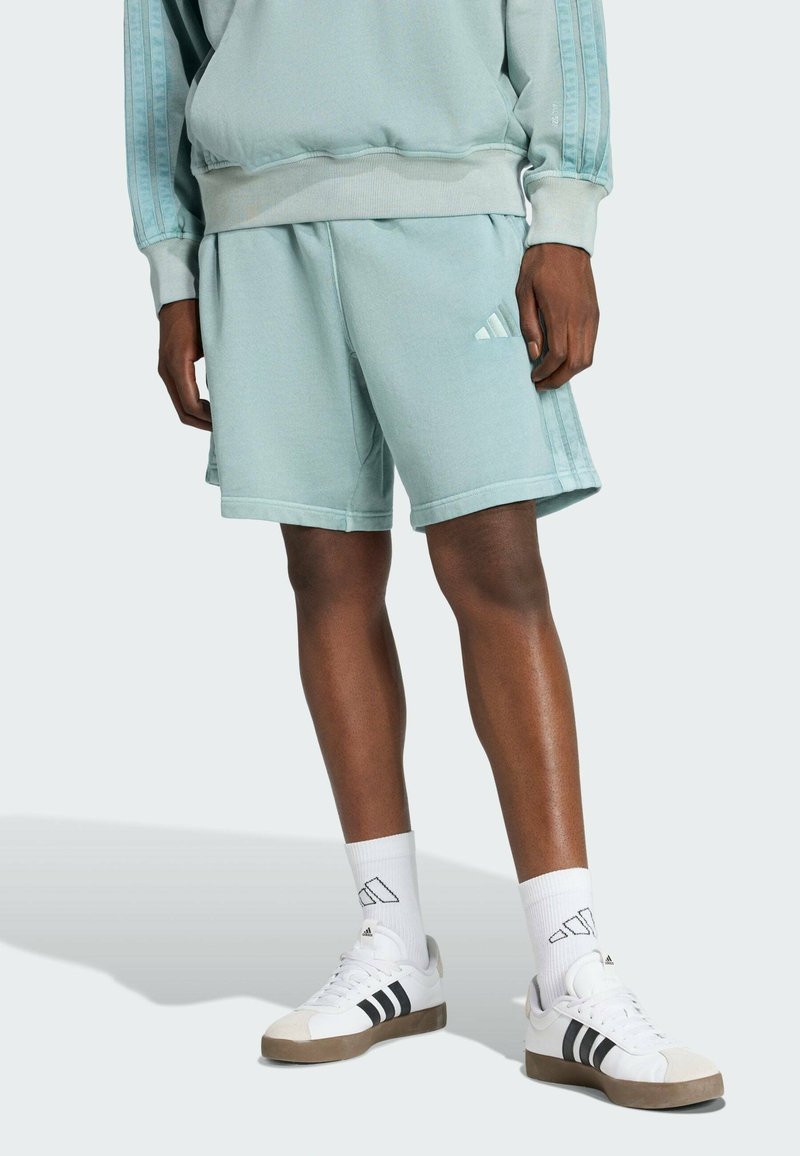 Jasnoniebieskie szorty sportowe z miękkiego materiału, z elastycznym paskiem w talii i białym logo adidas. W połączeniu z białymi butami i skarpetkami.