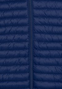 Veste matelassée navy avec un design en quilt, des coutures horizontales et une fermeture éclair sur toute la longueur au centre. Texture de tissu lisse et brillante.