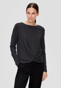 Langärmliges, dunkelgraues Oberteil mit rundem Ausschnitt, verdrehtem Vorderdesign und weicher Textur. Kombiniert mit schwarzen Hosen.