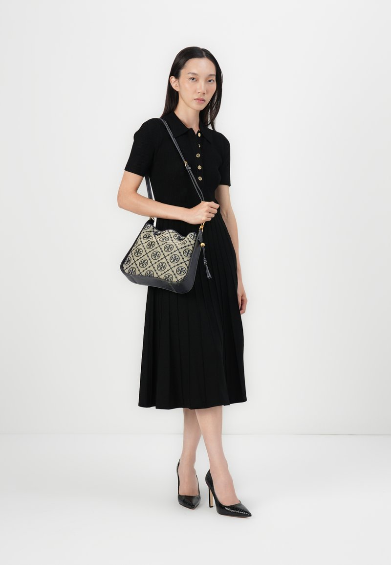 Schwarzes Faltenkleid mit einem geknöpften Kragen; Handtasche aus gemustertem Canvas in Creme und Marineblau, akzentuiert mit goldenen Beschlägen.