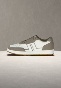 Λευκό και ταουπ sneaker χαμηλού προφίλ με διάτρητη μύτη, δέσιμο με κορδόνια και λαστιχένια σόλα σε ουδέτερη επιφάνεια και φόντο.