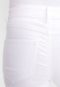 Jeans bianchi con una texture liscia, dotati di tasca posteriore e cuciture pulite. Il design include una silhouette aderente e vita media.