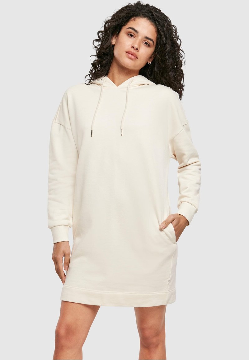 Gaiši bēšas kapuces sporta kleitas ar garām piedurknēm, sānu kabatām, ribotu aproču apdari un brīvu pieguļošos ar taisnu apakšmalu.