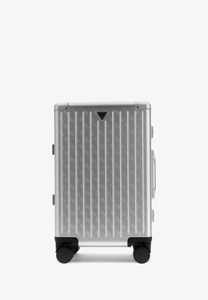 Silver hard-shell suitcase with vertical ridges, four black wheels, and a Guess logo on the front side.