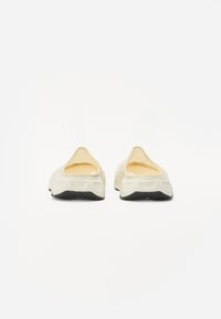 Ljust färgade slip-on skor med en slät, rundad ovandel, ett vadderat inre och en texturerad svart gummisula för grepp.