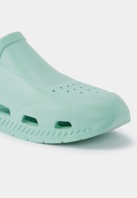 Calçado moldado verde-menta com orifícios de ventilação, uma textura suave e um design contornado, apresentando um salto ligeiramente elevado e sola estriada.