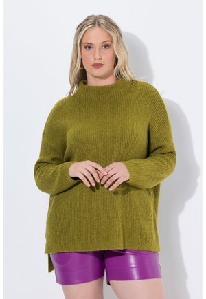Olivgrön stickad tröja med hög krage och lös passform, i kombination med glänsande lila shorts. Har sidoklyftor för ökad komfort.