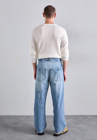 Ljusblå denimjeans med hög midja, vida ben och distinkt sömnad på bakfickorna. Bärs med en krämfärgad stickad tröja.