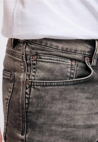Vaqueros de mezclilla gris deslavado con una textura suave, que presentan herrajes en tono cobre, cinco bolsillos y costuras a lo largo de las costuras.