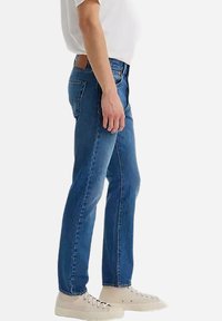 Jeans de mezclilla en azul medio con corte recto, que cuentan con un clásico diseño de cinco bolsillos y un ligero desvanecimiento a lo largo de los muslos.