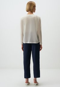 Lichtgewicht, sheer crème lange mouwtop met een ronde zoom, gecombineerd met navy straight-leg broek en witte open teen hakken. Eenvoudig ontwerp.