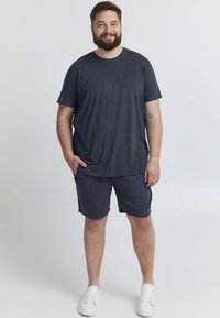 Tmavě šedé tričko s krátkým rukávem, doplněné o odpovídající kraťasy, vyrobené z měkké tkaniny. Bílé tenisky dokončují outfit.