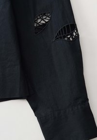 Black shirt sleeve with cut-out leaf designs, featuring a textured fabric, clean lines, and neat stitching along the hem.