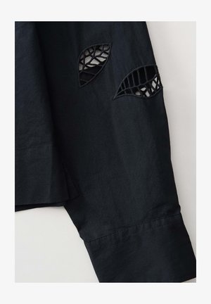 Manica di camicia nera con motivi a foglia ritagliati, caratterizzata da un tessuto testurizzato, linee pulite e cuciture ordinate lungo l'orlo.
