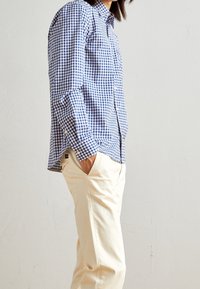 Blauw-wit geruite shirt met lange mouwen, knoopsluiting bij de kraag en borstzak; gecombineerd met crèmekleurige casual broek.