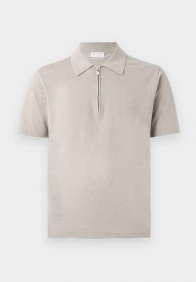 Μπεζ κοντομάνικο πόλο με μυτερό γιακά και μισό φερμουάρ μπροστά, απεικονίζεται σε μονόχρωμο φόντο.