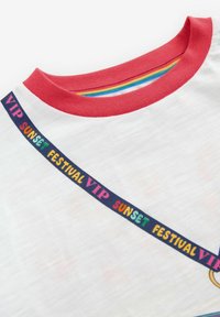 Balta kokvilnas t-krekls ar sarkanu apkakli, ar krāsainu tekstu "VIP SUNSET FESTIVAL" ap apkakli un daudzkrāsainu svītrainu iekšējo oderi.