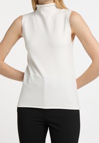 Weißes ärmelloses Oberteil mit einem Stehkragen und einem weichen, strukturierten Stoff. Das Design ist figurbetont und minimalistisch, ohne Muster oder Hardware.