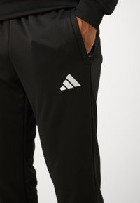 Calças de atletismo pretas feitas de tecido leve, com um cós elástico, bolsos laterais e um logótipo prateado da Adidas na coxa esquerda.
