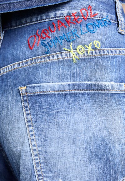 Denim-shortsit ovat vaaleansiniset ja niissä on kulunut pinta. Punaisilla, sinisillä ja keltaisilla värillä brodeerattu teksti lukee "DSQUARED2 KESÄN RAKASTAJAT XOXO."