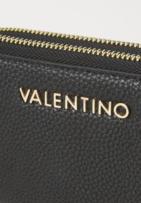 Schwarze, strukturierte Lederbörse mit einem goldenen Reißverschluss und geprägtem "VALENTINO"-Logo in goldener Schrift auf der Vorderseite.