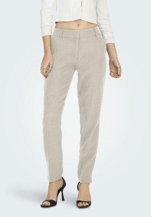 Pantalones beige ajustados con un corte slim, frente plano y lazos para cinturón. Tejido suave con una textura sutil, combinados con sandalias de tacón negro.