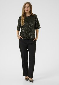 Melna, sekvīriem rotāta, īsām piedurknēm blūze kombinēta ar melniem pielāgotiem biksēm un svītrainiem papēžiem. Blūzei ir apaļš kakla izgriezums un brīvs piegriezums.