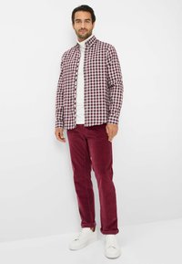 Camicia a maniche lunghe a scacchi color marrone e bianco, abbinata a pantaloni in velluto a coste bordeaux. Sneakers bianche completano l'outfit.