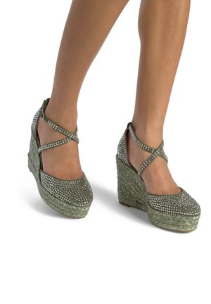 Green wedge shoes with a woven texture, embellished with rhinestones on the toe area and crisscross straps at the ankle.