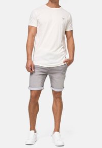 T-shirt blanc à manches courtes avec un petit logo, associé à un short en denim gris clair retroussé au bas, complété par des baskets blanches.