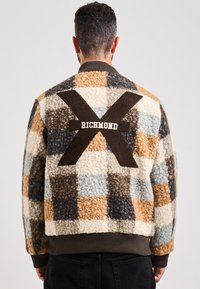 Giubbotto bomber a quadri fuzzy con tonalità marroni, beige, blu e crema, caratterizzato da una grande "X" marrone e dal logo "RICHMOND" sul retro.