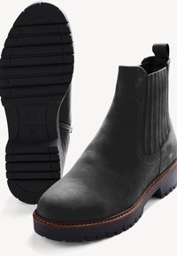 Botas Chelsea de cuero negro con paneles laterales texturizados, puntera redonda y suela de goma. Presentan una tira de agarre y un detalle de costura alrededor de la suela.