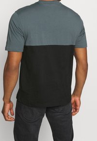 Camiseta de manga corta con diseño a bloques de color, presentando una sección superior en color teal y una sección inferior en negro. Fabricada con tela suave, tiene un ajuste casual.