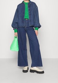 Jeansjacka med ballongärmar över en grön stickad tröja, tillsammans med vida jeans, beiga skor och en kviltad grön handväska.