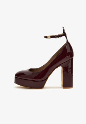 Escarpin plateforme à talon haut en cuir verni bordeaux, avec bout arrondi, bride à la cheville et boucle dorée. Texture lisse et brillante.