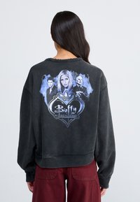 Felpa nera oversized con stampa grafica di tre personaggi di "Buffy l'ammazzavampiri" in tonalità di blu su uno sfondo solido.