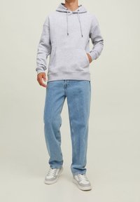Felpa grigia con cappuccio e tasca frontale. Jeans baggy blu chiaro. Sneakers grigie e bianche con accenti sottili. Design semplice e casual.