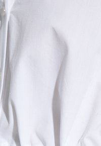 Tessuto di cotone bianco con una texture liscia, che presenta pieghe sottili e un dettaglio a bottone, mostrando un design semplice e pulito.