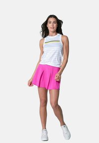 Top senza maniche a righe bianche con accenti gialli e verdi, abbinato a una gonna plissettata rosa. Il modello indossa scarpe sportive bianche.