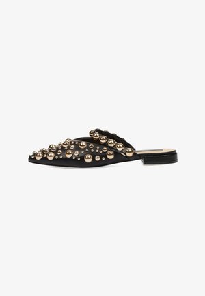 Zapato negro tipo slip-on con cuentas metálicas doradas de diversos tamaños, punta afilada, tela texturizada y tacón cuadrado bajo.