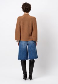 Bruine geribde trui met hoge hals, gecombineerd met blauwe denim culottes en zwarte kniehoog laarzen, gezien vanaf de achterkant.