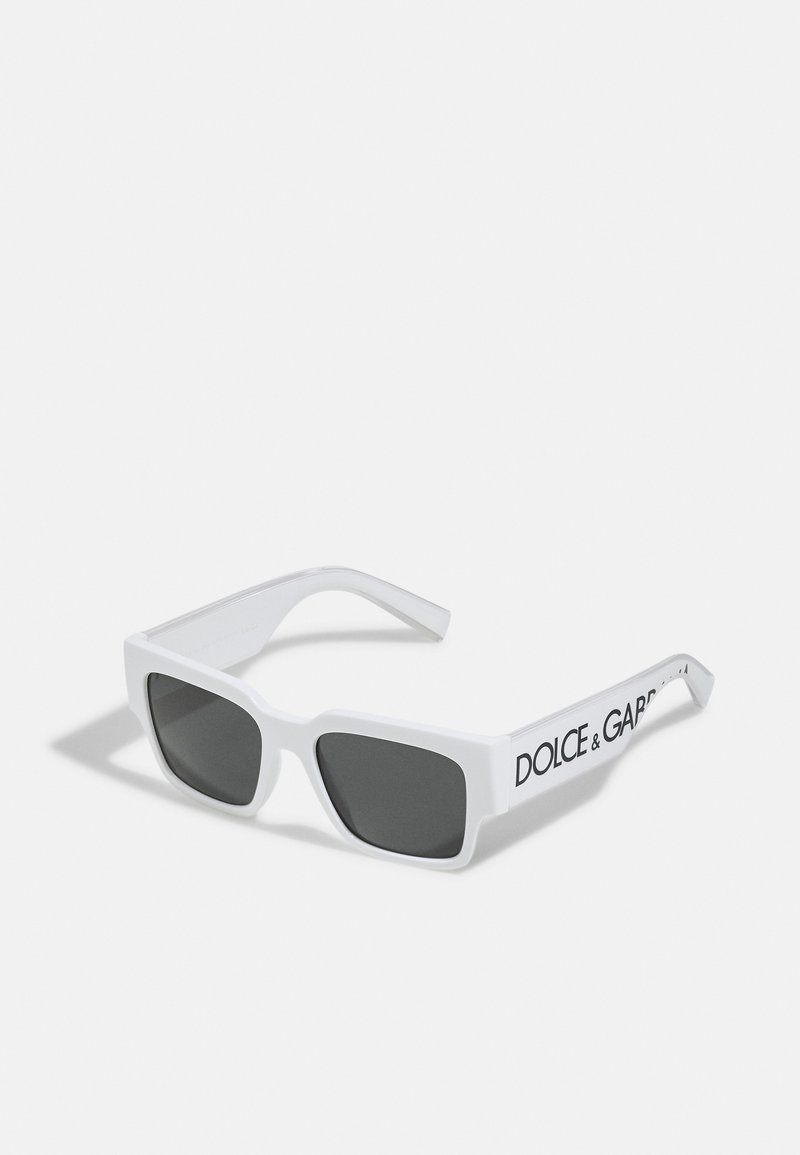Baltas kvadrāta formas saulesbrilles ar pelēkiem stikliem. Masīva plastmasas rāmja dizains, kurā uz uzlikām melnā krāsā ir redzams zīmola nosaukums "DOLCE & GABBANA".