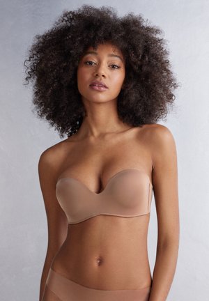 Beige strapless bh gemaakt van een gladde stof met voorgevormde cups en subtiele naden. Het ontwerp is minimalistisch en heeft een lage uitsnede.