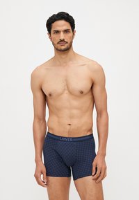 Navy patterned boxers with elastic waistband featuring "Levi's" branding. Material appears smooth with a fitted design and mid-thigh length.